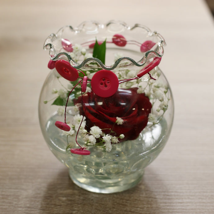 Small flower arrangement. One red rose surrounded but babies breath. The vase is clear and has a tie around the top. 